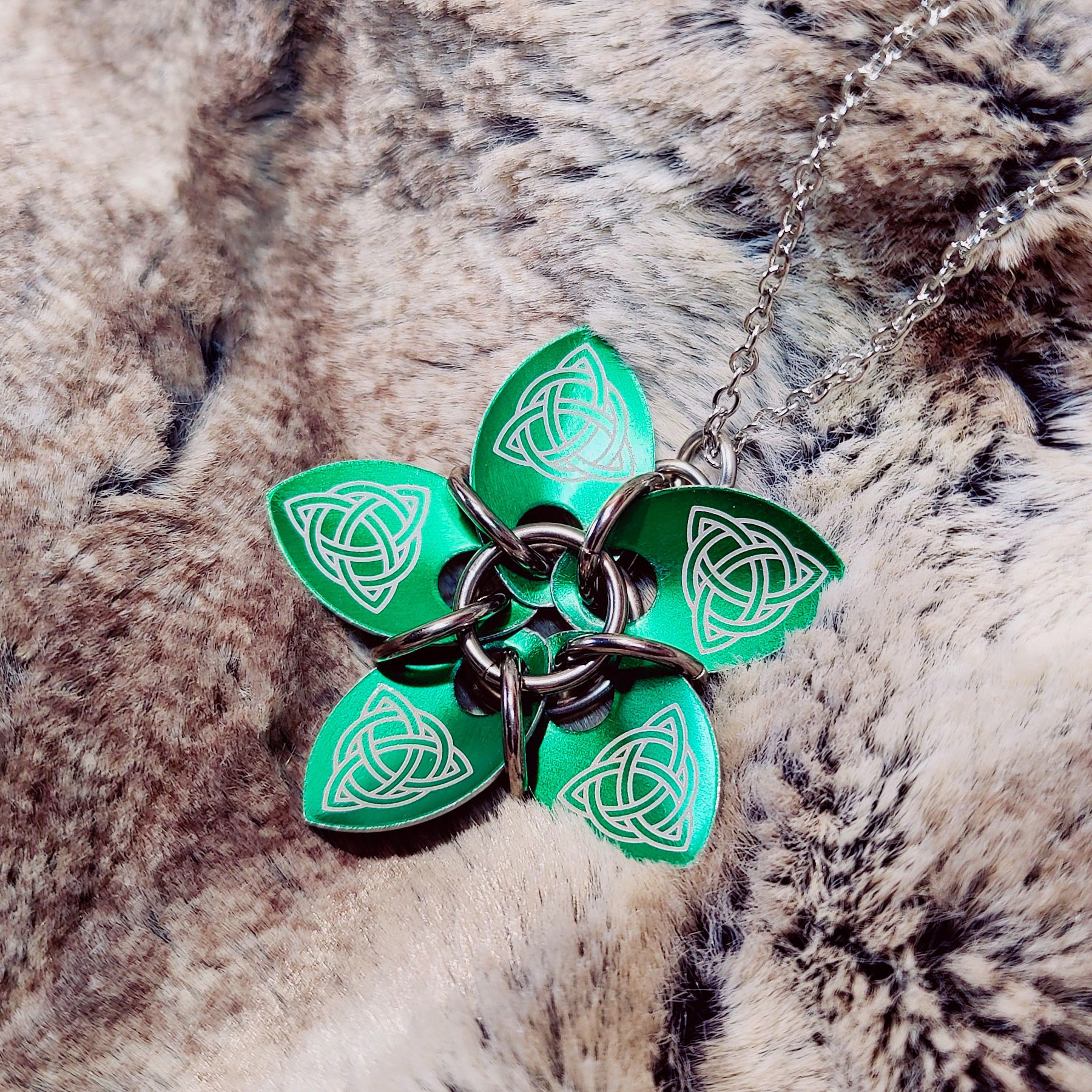 Les quatre photos montrent des pendentifs similaires : ils sont composés de plusieurs écailles qui forment une fleur, retenues par des anneaux. Ici, la fleur est vertes avec des motifs celtiques.